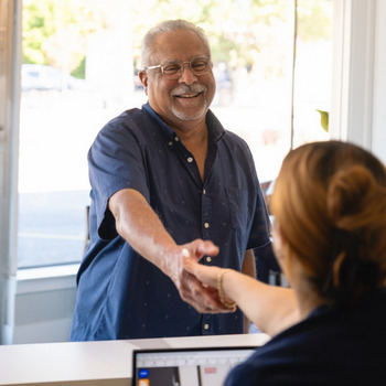 A man is smiling and shaking hands with the receptionist at Hylan Dental Care